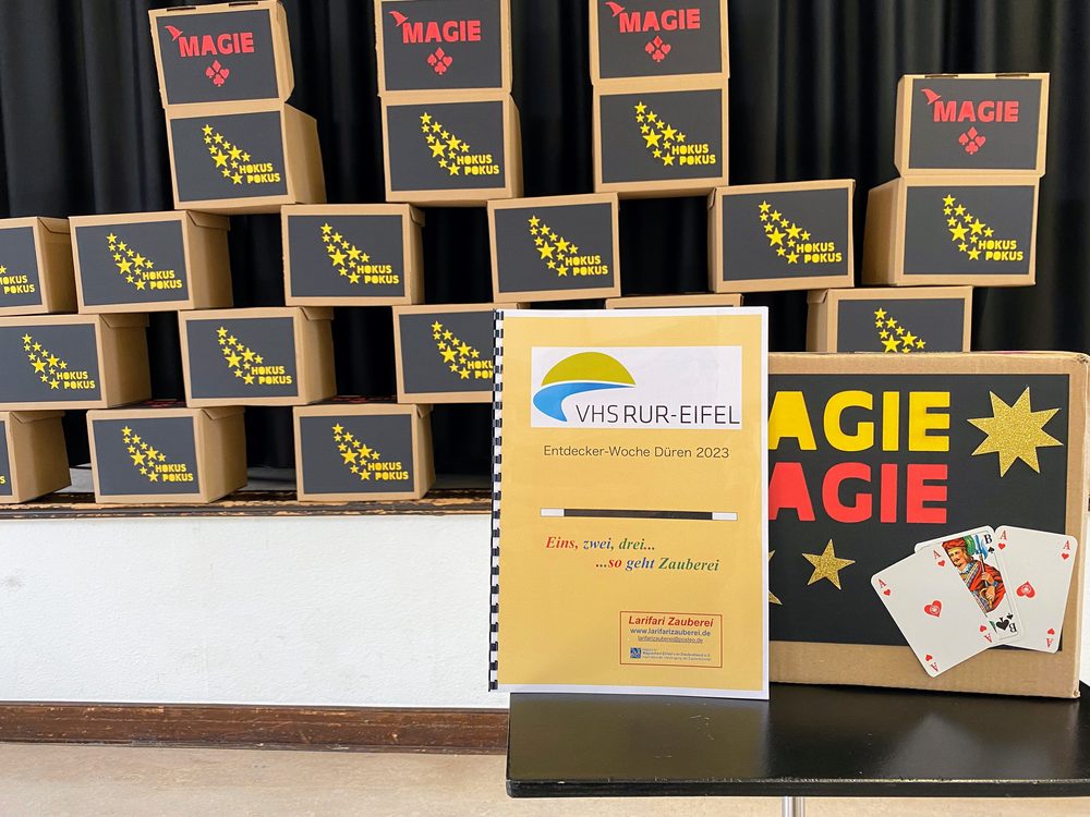 Gestapelte selbstgebaute Zauberkästen mit der Aufschrift Magie und Hokus Pokus, davor das Kursheft.